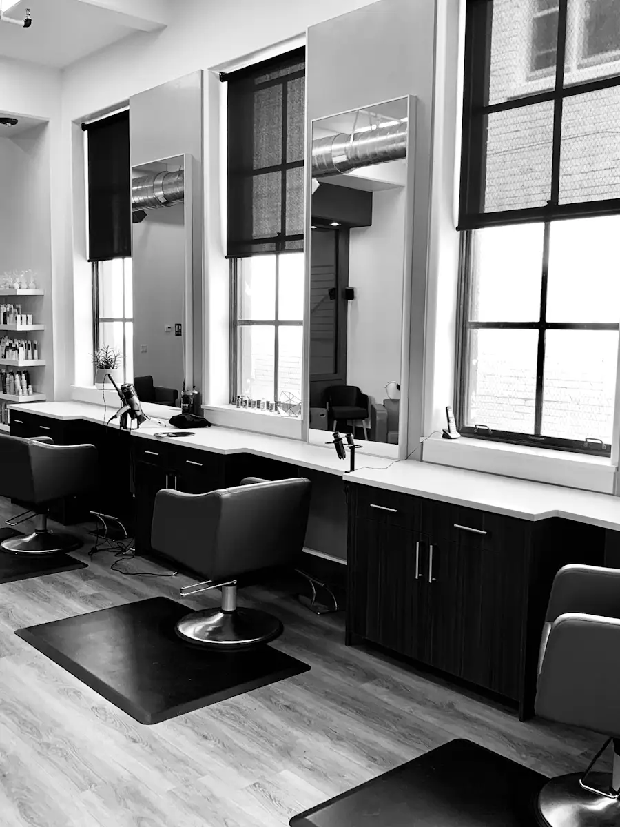 Interno del salone in bianco e nero: postazioni allineate davanti a grandi finestre