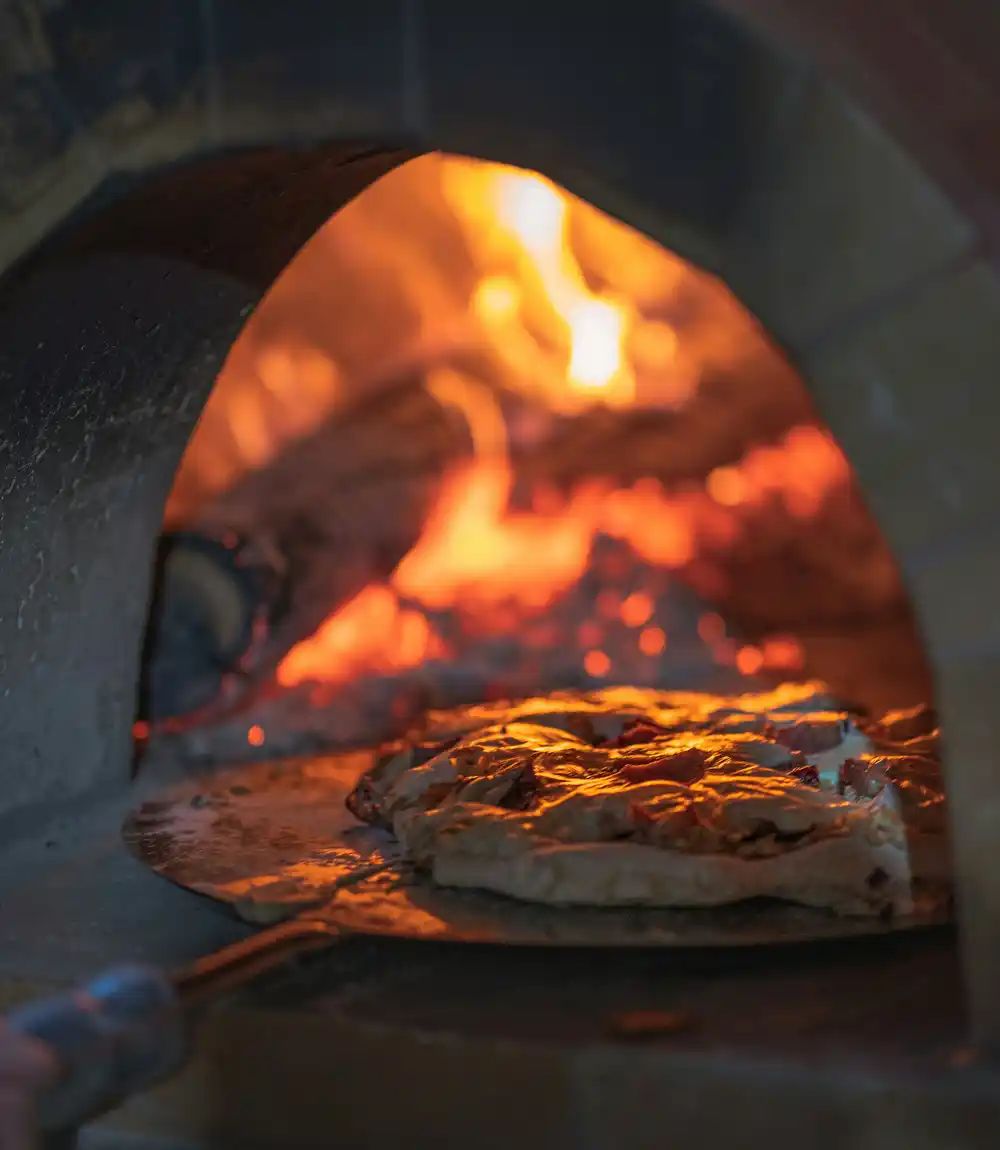 Una pizza infornata nel forno a legna, con la fiamma viva sul fondo