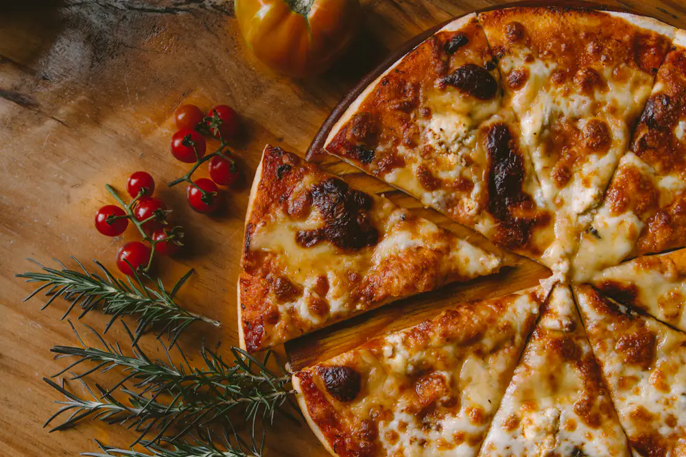 Pizza appena sfornata su un tagliere di legno, con pomodorini e rosmarino accanto