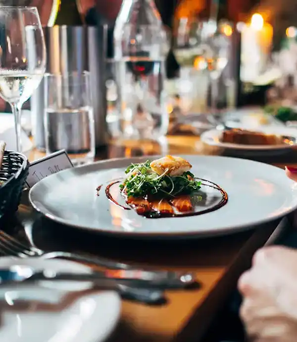 Un piatto servito al tavolo, con i calici di vino e il cestino del pane accanto