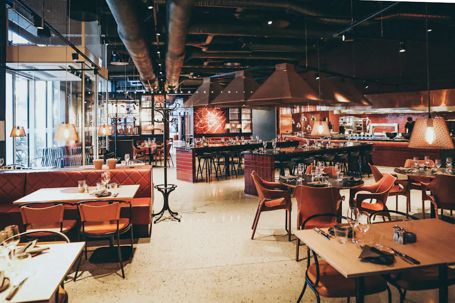 Sala del locale con tavoli in legno, sedute rosse e la cucina a vista sul fondo